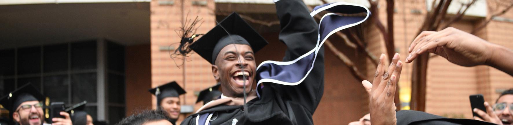 Graduate laughs as he is lifted up by his fellow graduates